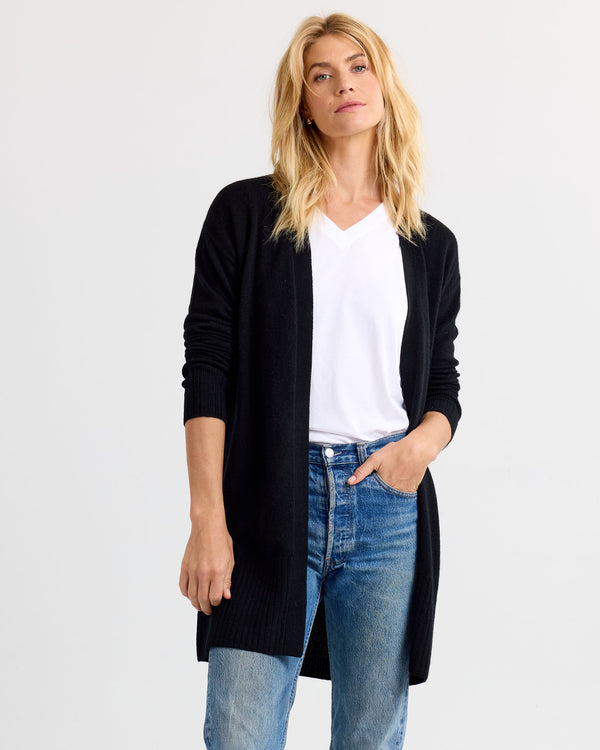 LIFESTYLE / EDITORIAL: Woman wearing black long cashmere cardigan, white V-neck shirt, and blue jeans against white