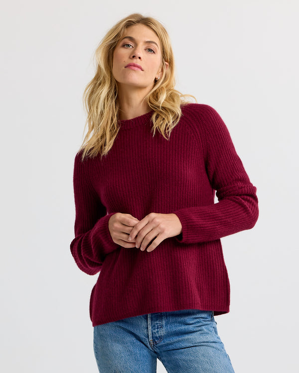 LIFESTYLE / EDITORIAL: Woman wearing a burgundy ribbed cashmere sweater and blue jeans against a plain background