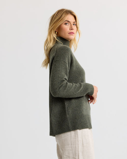 Dark olive cashmere funnel neck sweater with light trousers, side view