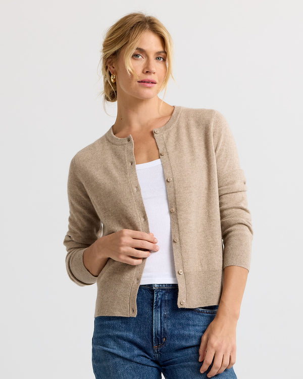 Woman wearing driftwood beige cashmere cardigan over white tank top and blue jeans against a plain background