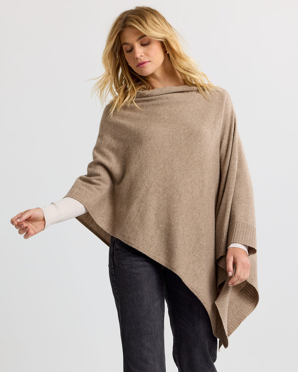 LIFESTYLE / EDITORIAL: Woman wearing asymmetrical beige cashmere poncho with black pants against plain background