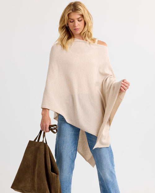 LIFESTYLE / EDITORIAL: Woman wearing oatmeal cashmere poncho with one shoulder exposed, holding brown suede tote bag