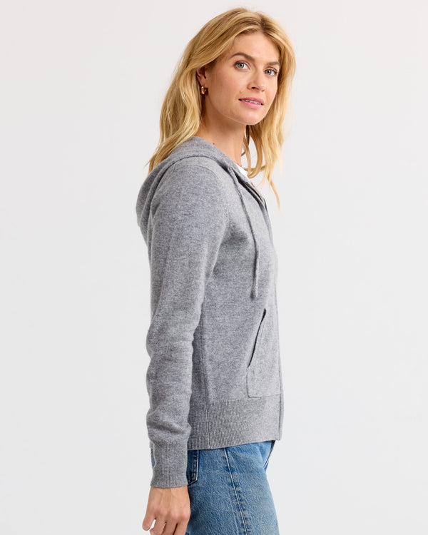 LIFESTYLE / EDITORIAL: Woman wearing grey cashmere hoodie and blue jeans, standing sideways against white background