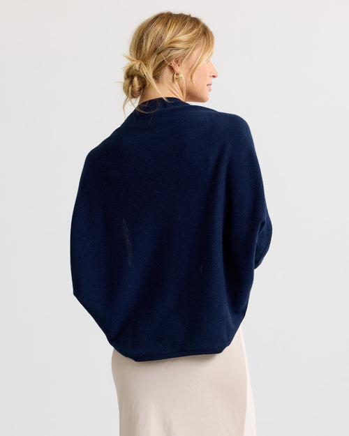 LIFESTYLE / EDITORIAL: Woman wearing navy cashmere sweater, back view, with beige skirt and hair in low bun against white