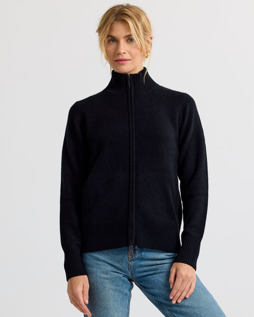 LIFESTYLE / EDITORIAL: Woman wearing black zip-up cashmere sweater and blue jeans against plain background
