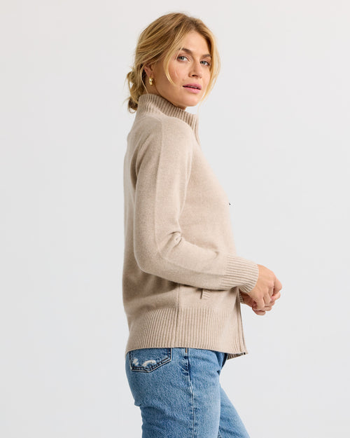LIFESTYLE / EDITORIAL: Woman in beige cashmere turtleneck sweater and blue jeans, side view, neutral background