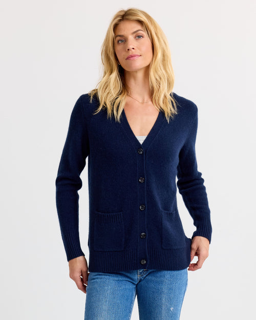 Woman wearing navy cashmere cardigan with pockets and buttons, paired with blue jeans against white background