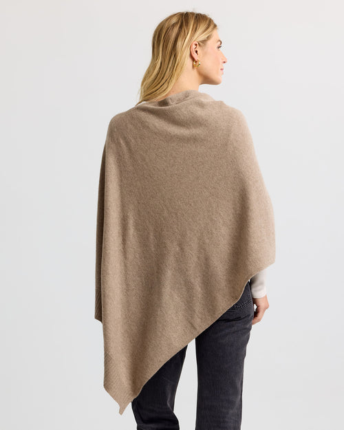LIFESTYLE / EDITORIAL: Woman wearing driftwood-colored cashmere poncho, viewed from back against plain background