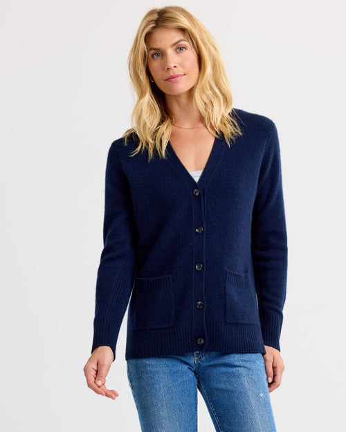 LIFESTYLE / EDITORIAL: Woman wearing navy cashmere cardigan with pockets and buttons, paired with blue jeans against white