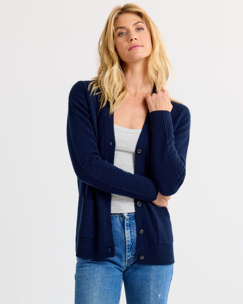 LIFESTYLE / EDITORIAL: Woman wearing navy cashmere cardigan over gray tank top and blue jeans against white background