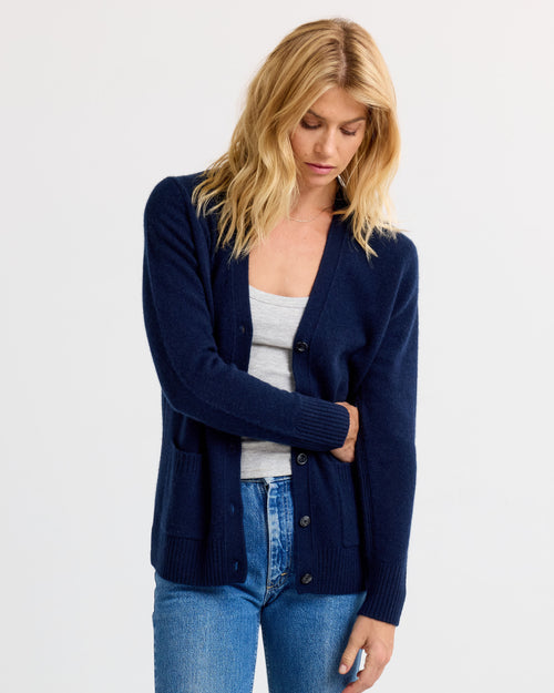 Three-quarter view image of a woman wearing a navy cashmere cardigan over a gray tank top and blue jeans.