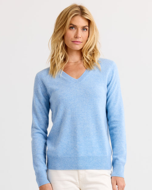Woman wearing light blue V-neck cashmere sweater and white pants, standing against plain white background