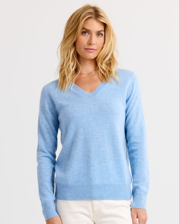 Woman wearing light blue V-neck cashmere sweater and white pants, standing against plain white background
