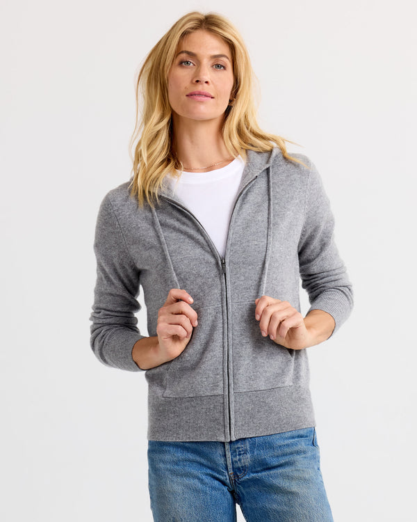 Front view image of a woman wearing a grey zip-up cashmere hoodie with a white tee and blue jeans