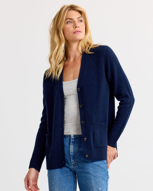LIFESTYLE / EDITORIAL: Woman wearing navy buttoned cashmere cardigan over gray tank top and blue jeans against white