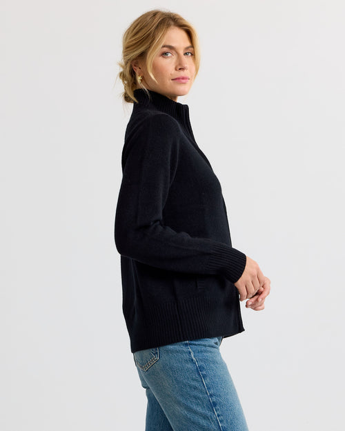 LIFESTYLE / EDITORIAL: Woman in black zip-up cashmere sweater and blue jeans, side view, neutral background