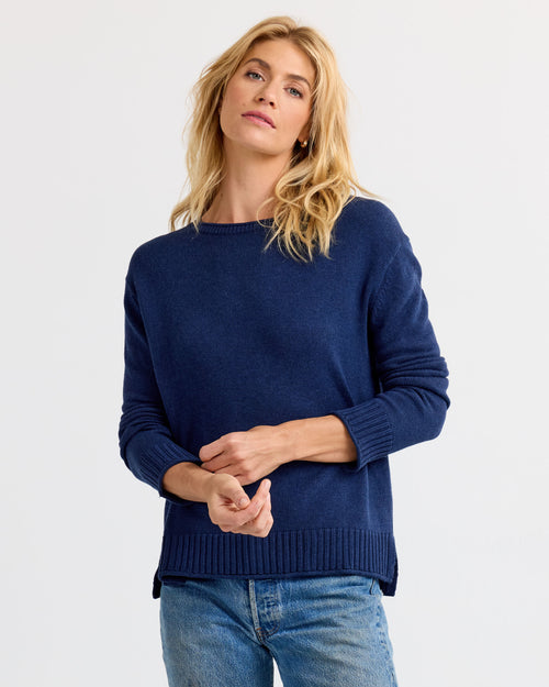 LIFESTYLE / EDITORIAL: Woman wearing navy blue cashmere sweater and jeans, standing against plain white background