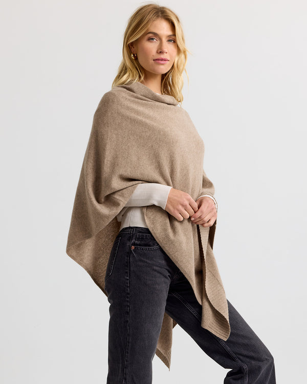 Three-quarter view image of a woman wearing a driftwood cashmere poncho paired with black jeans against white backdrop