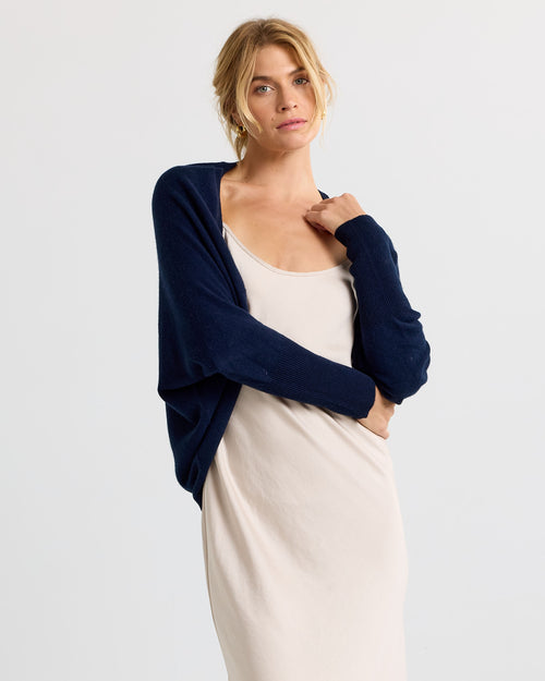 Three-quarter view image of a woman wearing a navy cashmere cardigan over a beige slip dress with arms crossed