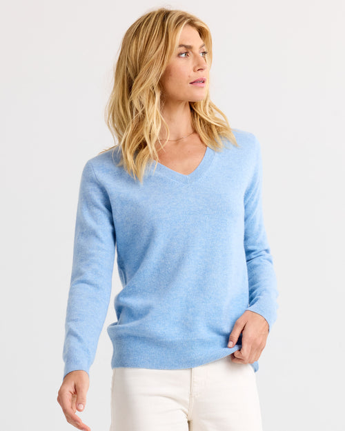 LIFESTYLE / EDITORIAL: Woman wearing light blue V-neck cashmere sweater and white pants, looking to the side against white