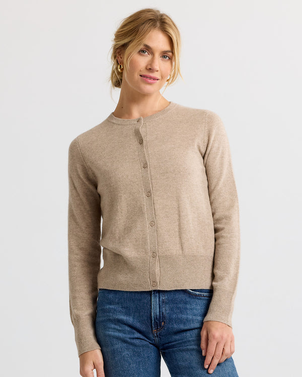 Front view image of a woman wearing a beige cashmere cardigan buttoned up with blue jeans against a plain background