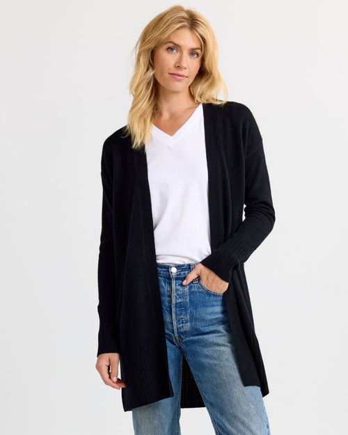 LIFESTYLE / EDITORIAL: Woman wearing black open-front cashmere cardigan, white V-neck shirt, and blue jeans against white