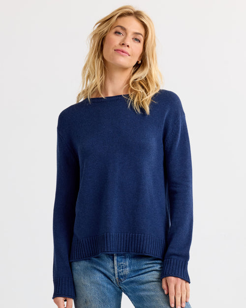 Front view image of a woman wearing a navy blue cashmere sweater with blue jeans against a white backdrop