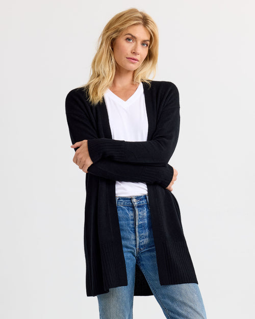 LIFESTYLE / EDITORIAL: Woman wearing black long cashmere cardigan over white shirt and blue jeans against white background