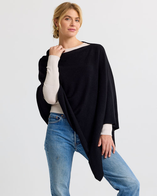 LIFESTYLE / EDITORIAL: Woman wearing black cashmere poncho over cream sweater and blue jeans against white background