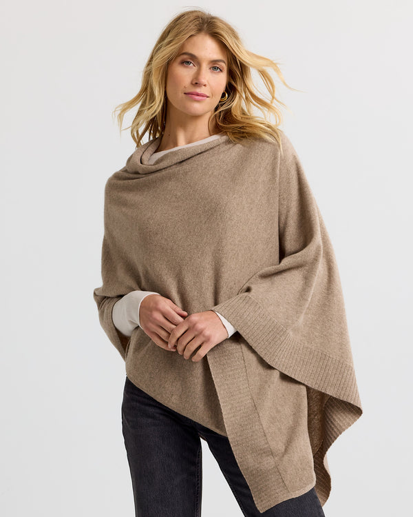 LIFESTYLE / EDITORIAL: Woman wearing a driftwood-colored cashmere poncho over a light top and dark pants against a plain