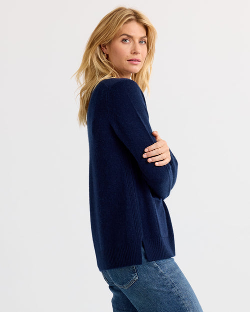 LIFESTYLE / EDITORIAL: Woman in navy blue cashmere sweater and jeans, posed sideways against plain background