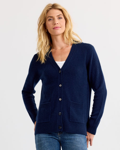 Front view image of a woman wearing a navy cashmere cardigan with pockets over a white top and blue jeans