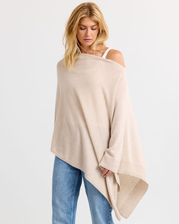 LIFESTYLE / EDITORIAL: Woman wearing oatmeal cashmere poncho over one shoulder with blue jeans against white background