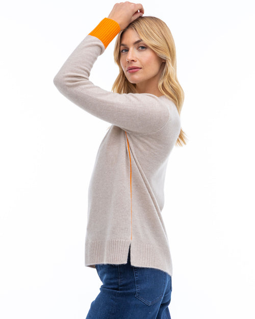 LIFESTYLE / EDITORIAL: Woman in beige cashmere sweater with orange cuffs posing sideways against white background