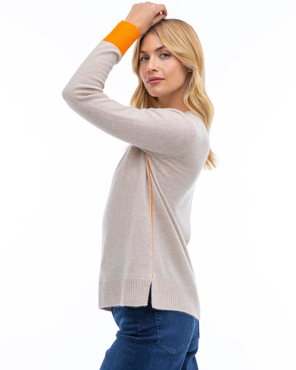 LIFESTYLE / EDITORIAL: Woman in beige cashmere sweater with orange cuffs posing sideways against white background