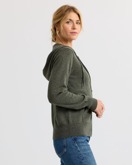 Woman in dark olive cashmere hoodie and blue jeans, side view, neutral background