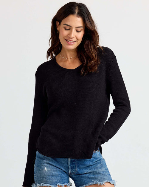 LIFESTYLE / EDITORIAL: Woman wearing black cashmere sweater and blue denim shorts, standing against white background