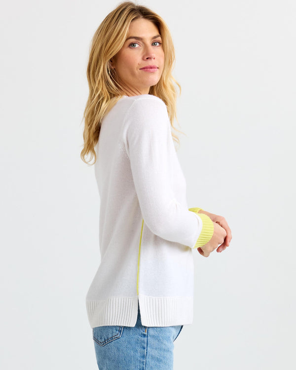 LIFESTYLE / EDITORIAL: Woman wearing white cashmere sweater with yellow cuffs and blue jeans, standing sideways against