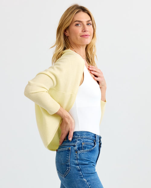 LIFESTYLE / EDITORIAL: Woman in white top, blue jeans, and light yellow cashmere shrug against white background