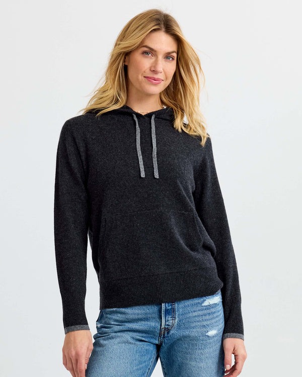Woman wearing charcoal gray cashmere hoodie sweater and blue jeans against plain background