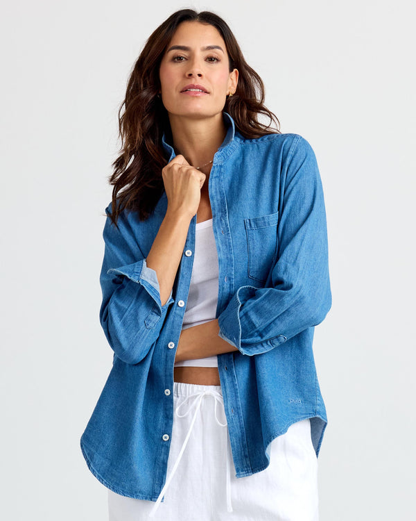 LIFESTYLE / EDITORIAL: Woman wearing medium wash denim shirt over white top and white pants against plain background