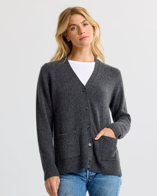 LIFESTYLE / EDITORIAL: Woman wearing charcoal grey cashmere cardigan over white top and blue jeans against plain background