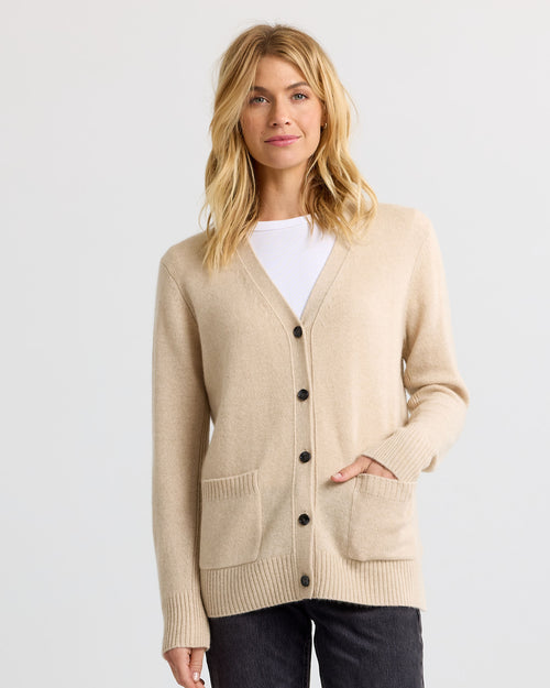 Woman wearing sandstone beige cashmere cardigan with front pockets and black buttons over white top