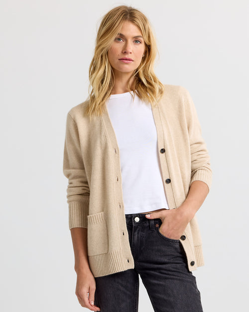Woman wearing sandstone beige cashmere cardigan over white tee and black jeans against plain light background