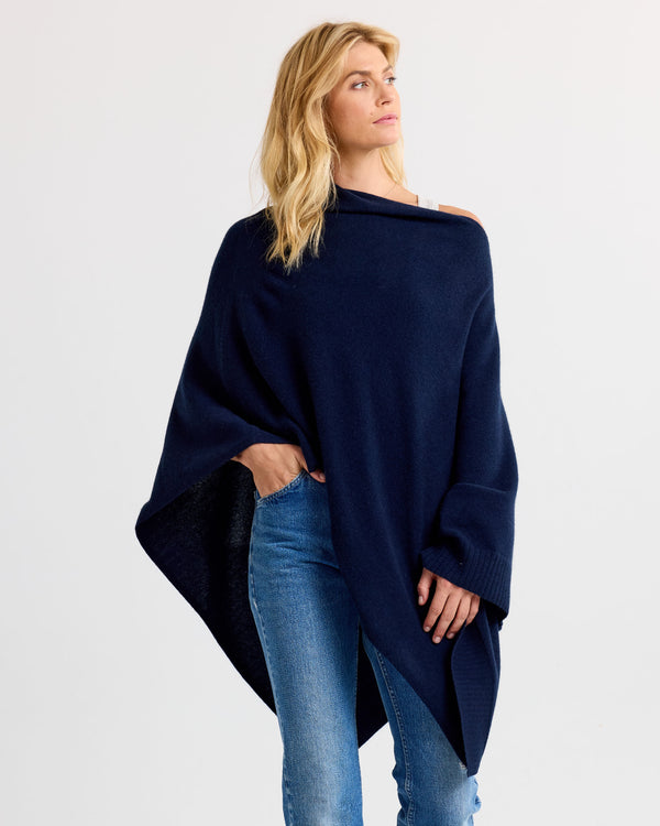 Woman wearing navy cashmere poncho with blue jeans against plain background