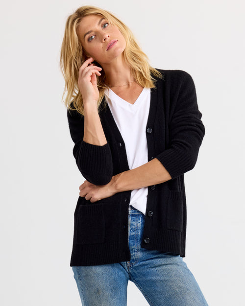 LIFESTYLE / EDITORIAL: Woman wearing black cashmere cardigan over white tee and blue jeans against plain background