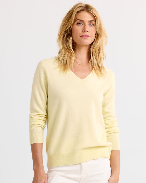 LIFESTYLE / EDITORIAL: Woman wearing a light yellow V-neck cashmere sweater and white pants against a plain background