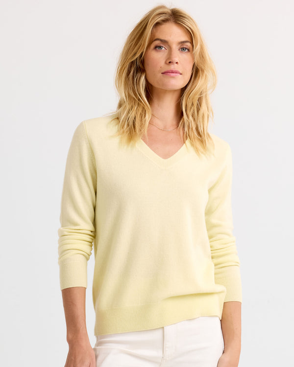 LIFESTYLE / EDITORIAL: Woman wearing a light yellow V-neck cashmere sweater and white pants against a plain background