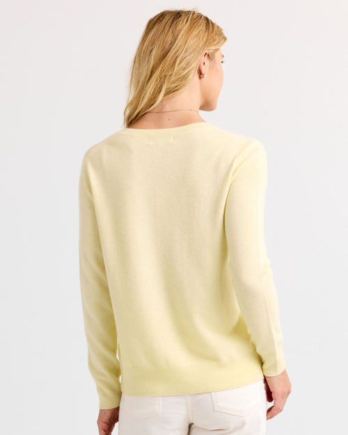 Woman wearing buttermilk yellow cashmere sweater, back view, paired with white pants against plain background