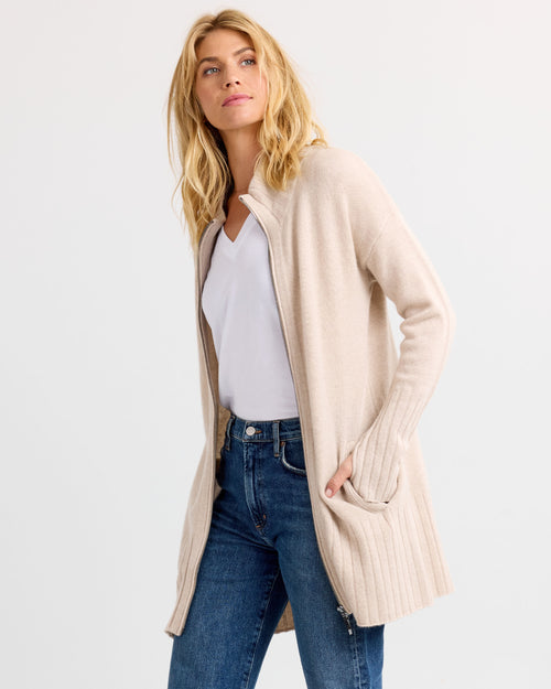 Three-quarter view image of a woman wearing oatmeal zip-up cashmere cardigan with pockets over white top and jeans